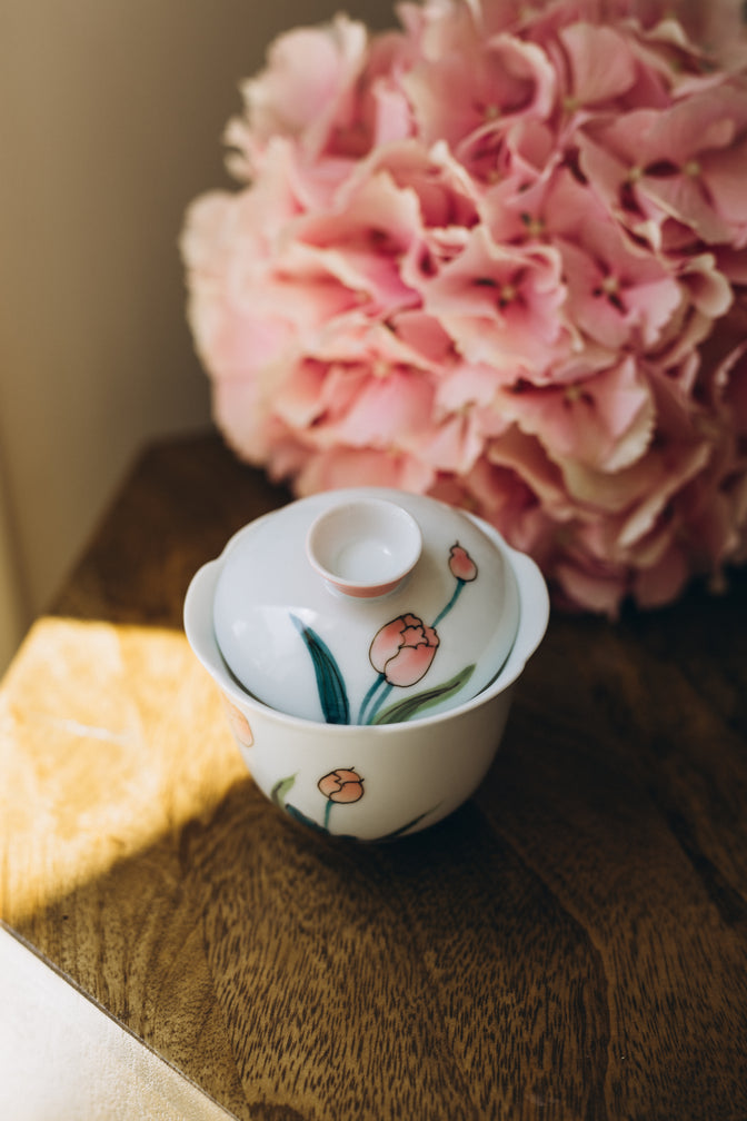 Pink Tulip gaiwan with its lid resting inside the bowl beside pink hydrangeas.