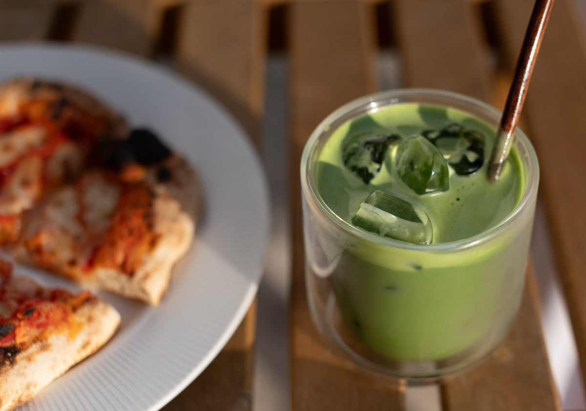 Iced matcha in a clear glass next to slices of pizza 