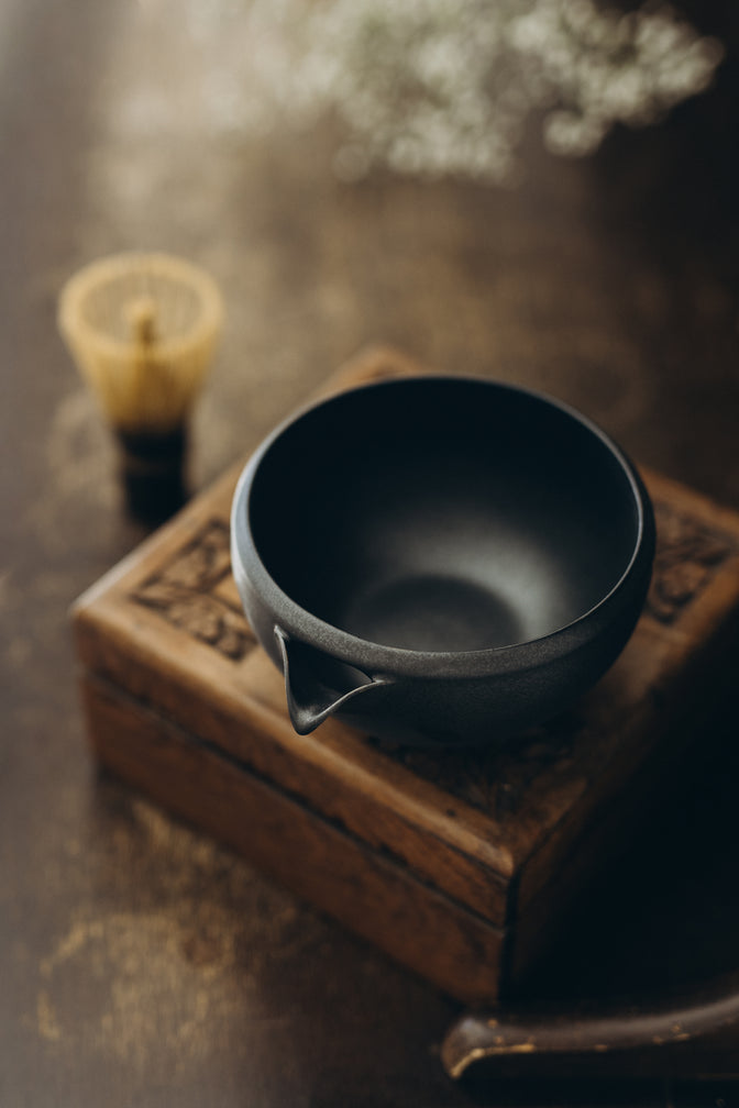 Black matcha bowl on wooden furniture in natural light.