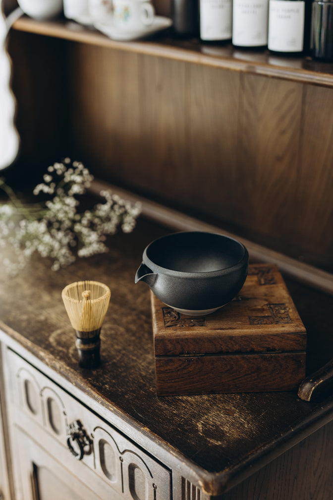 Black matcha bowl on wooden furniture in natural light.
