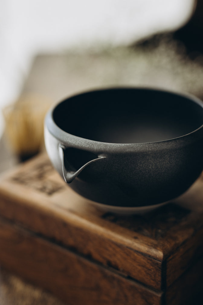 Black matcha bowl on wooden furniture in natural light.