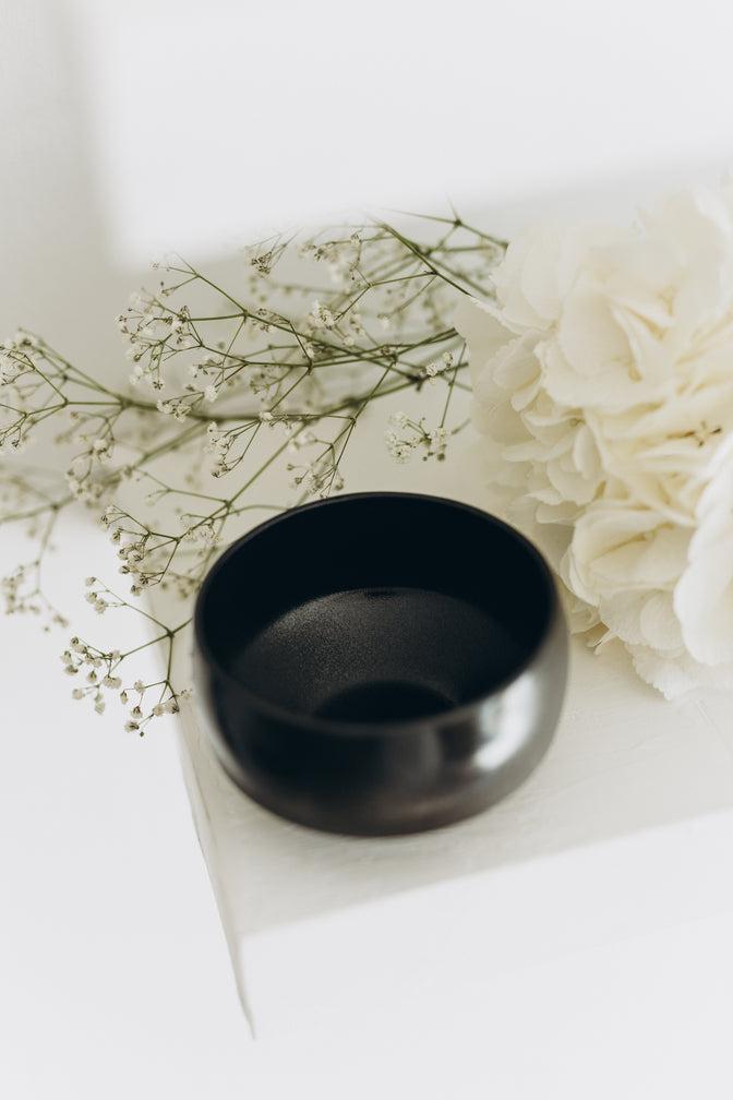 Black traditional matcha bowl viewed from above at an angle on a light shelf.