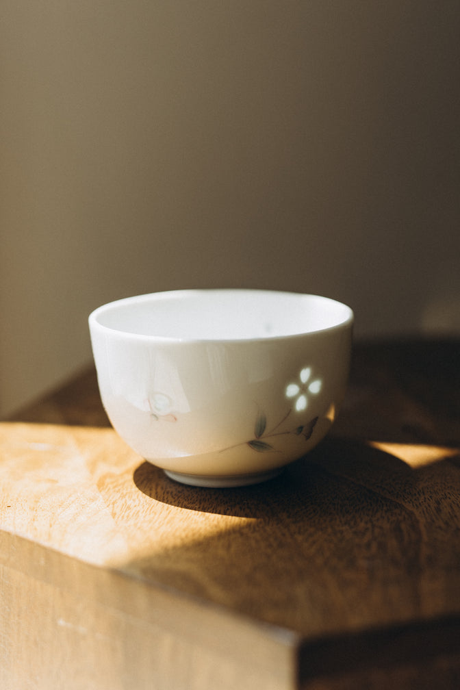 Dayflower porcelain teacup with translucent floral details on a wooden shelf.