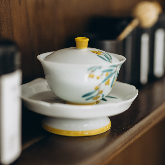 Japanese Plums gaiwan with a yellow lid knob and floral saucer on a wooden shelf.